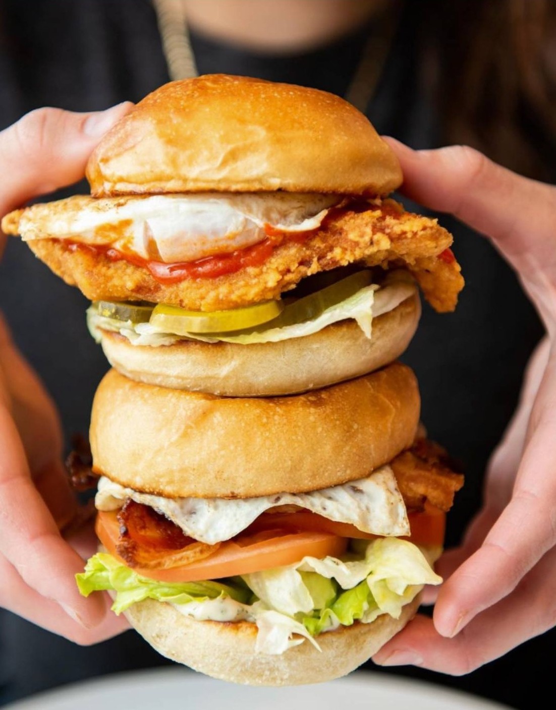Hands holding two stacked CHIX fried chicken and egg breakfast sandwiches